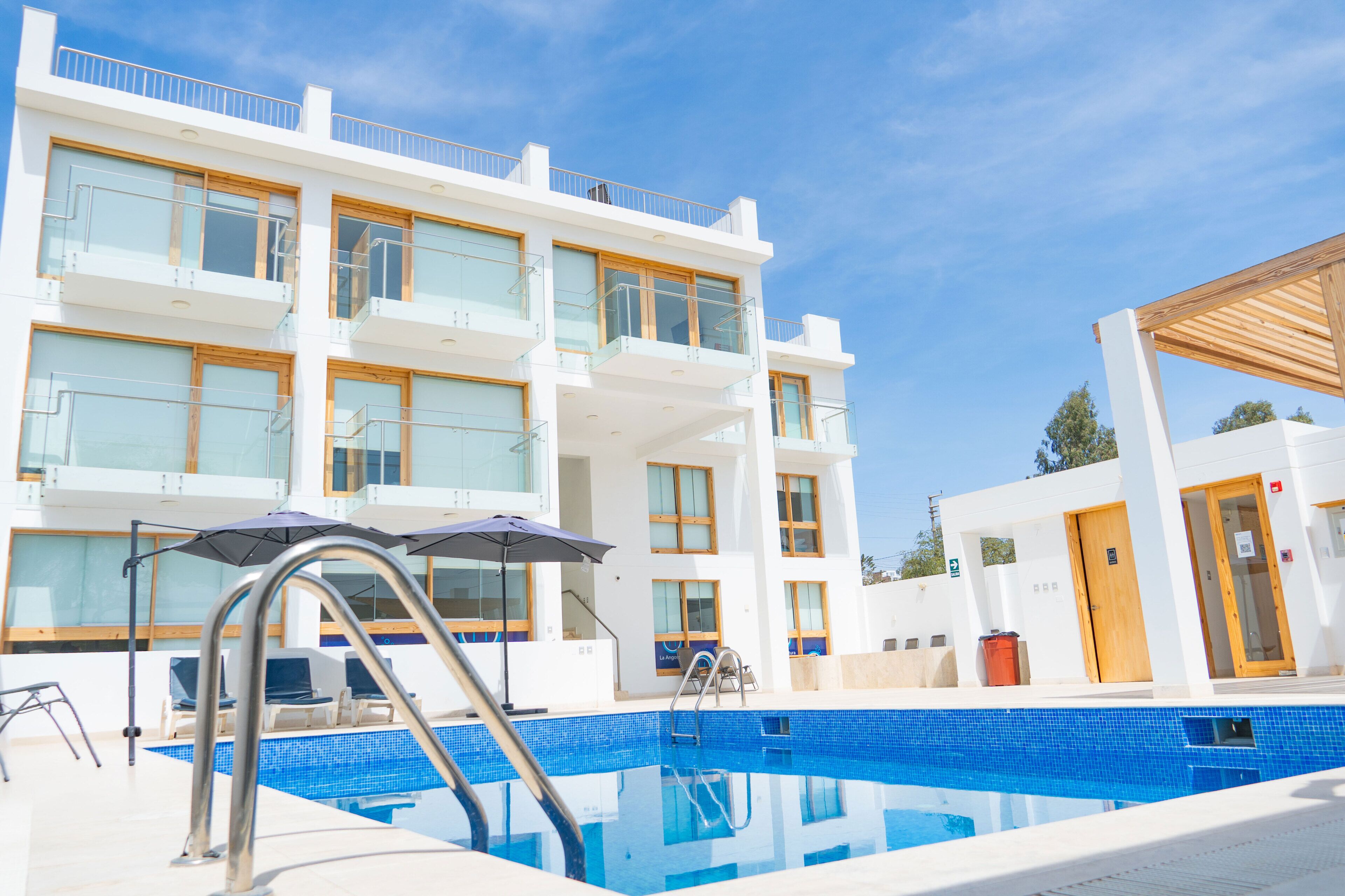 A modern hotel with a pool, multiple balconies, and a clear blue sky.