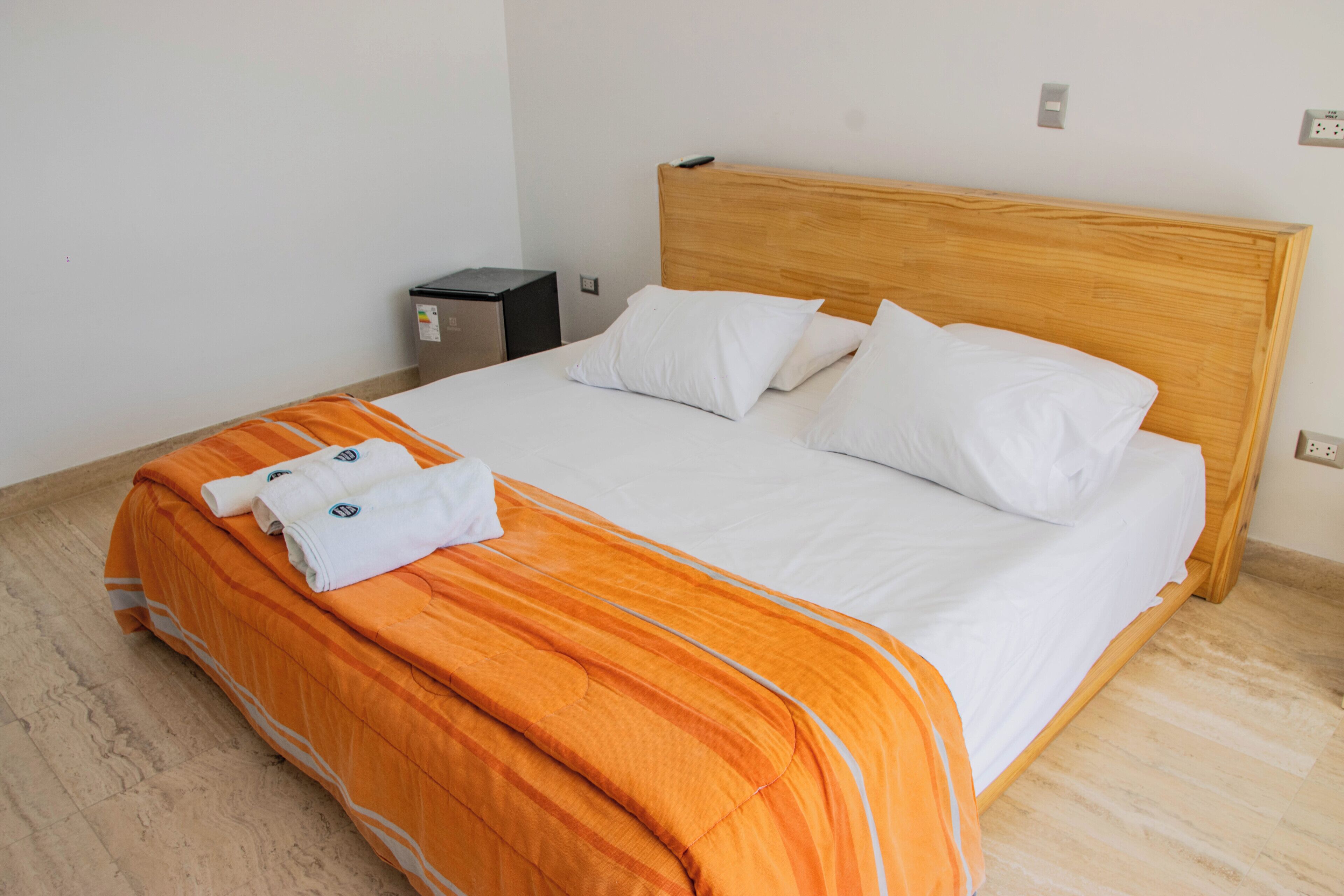 Un lit bien fait, avec une couvre-lit orange, des oreillers blancs et une tête de lit en bois.