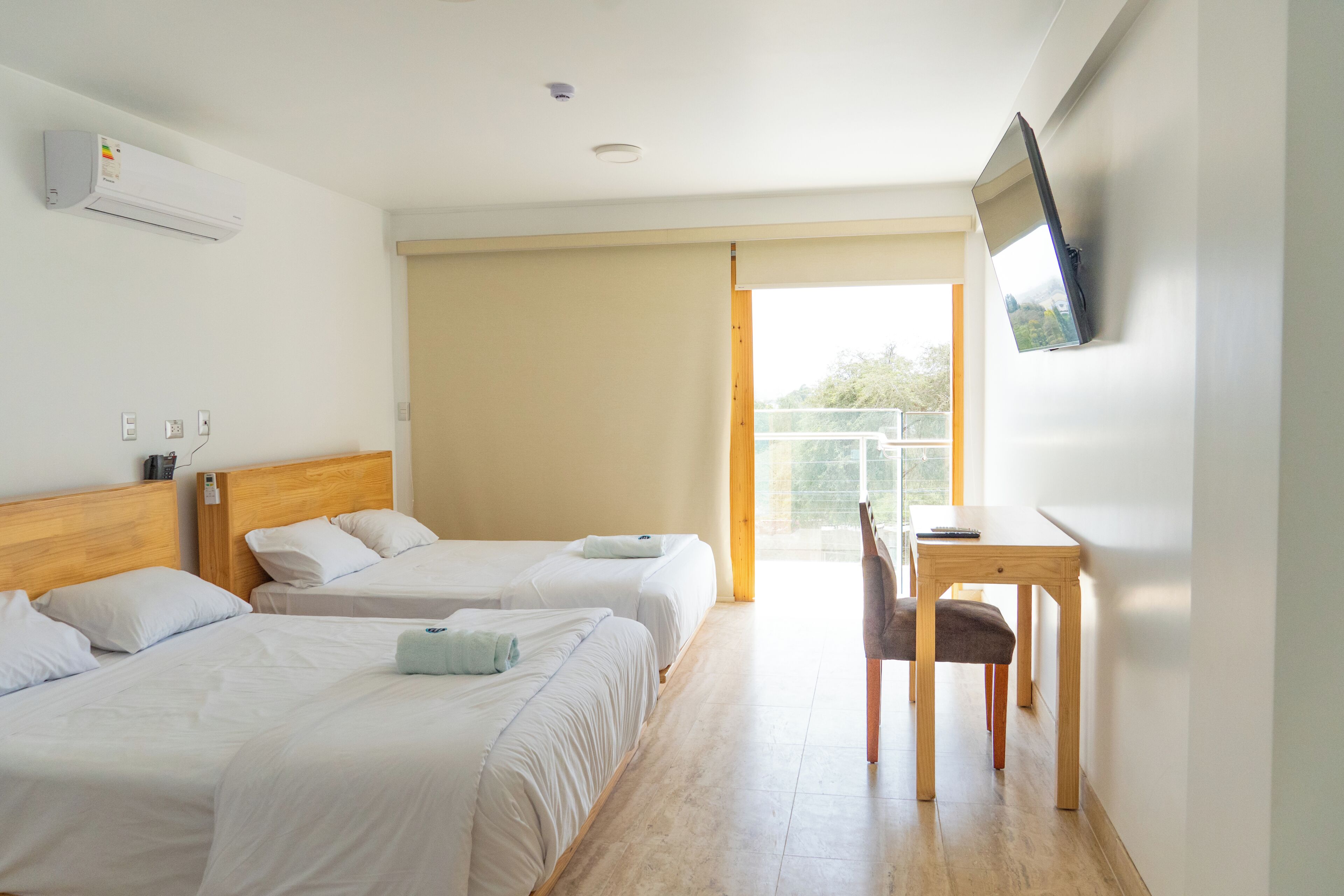 Une chambre d’hôtel avec deux lits, un bureau, une chaise, un téléviseur fixé au mur et une grande fenêtre.