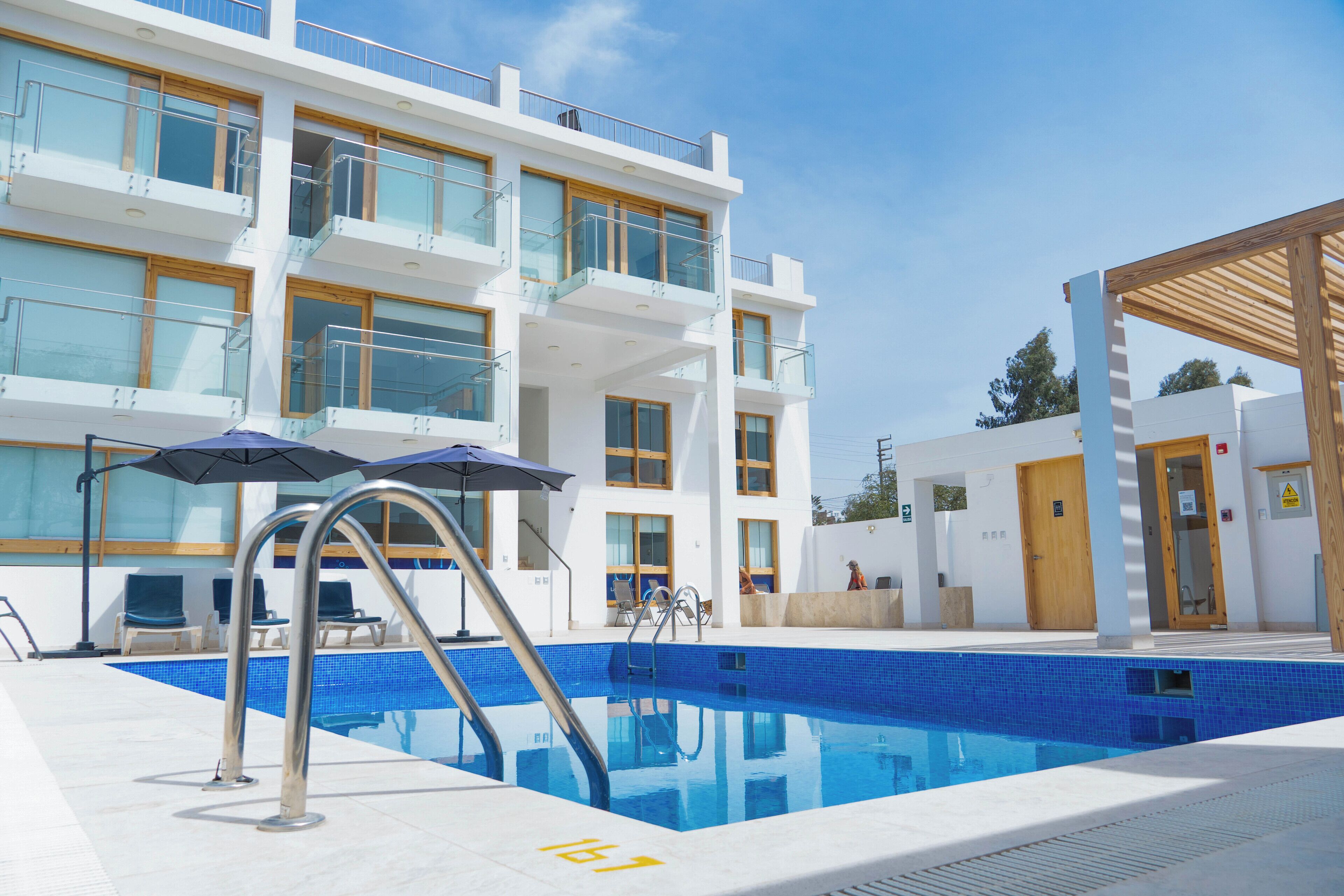 Un hotel moderno con piscina, varios balcones y mobiliario para exteriores.