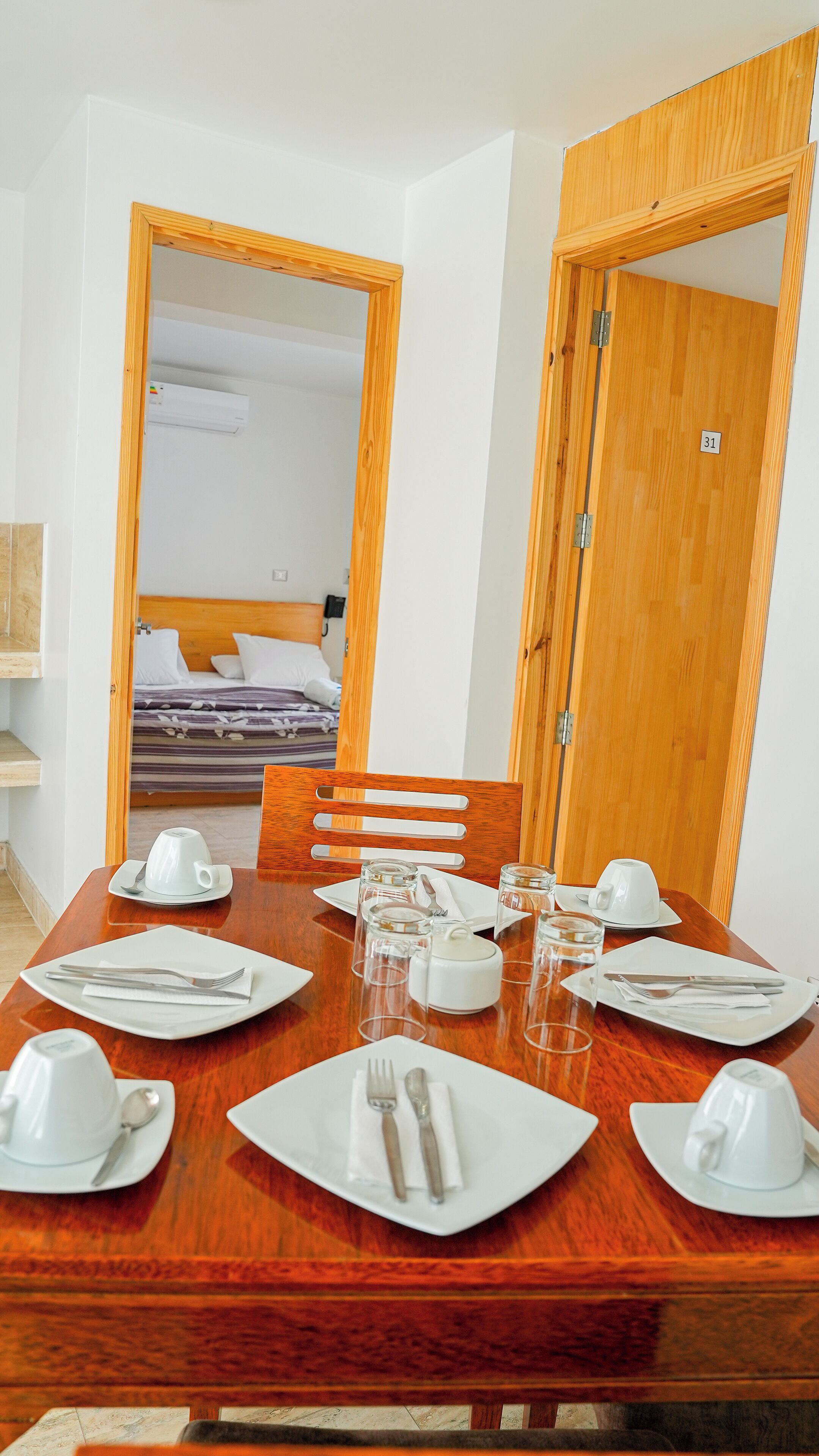 A dining table set with white plates, cutlery, and glasses, with a wooden chair and a wooden door in the background.
