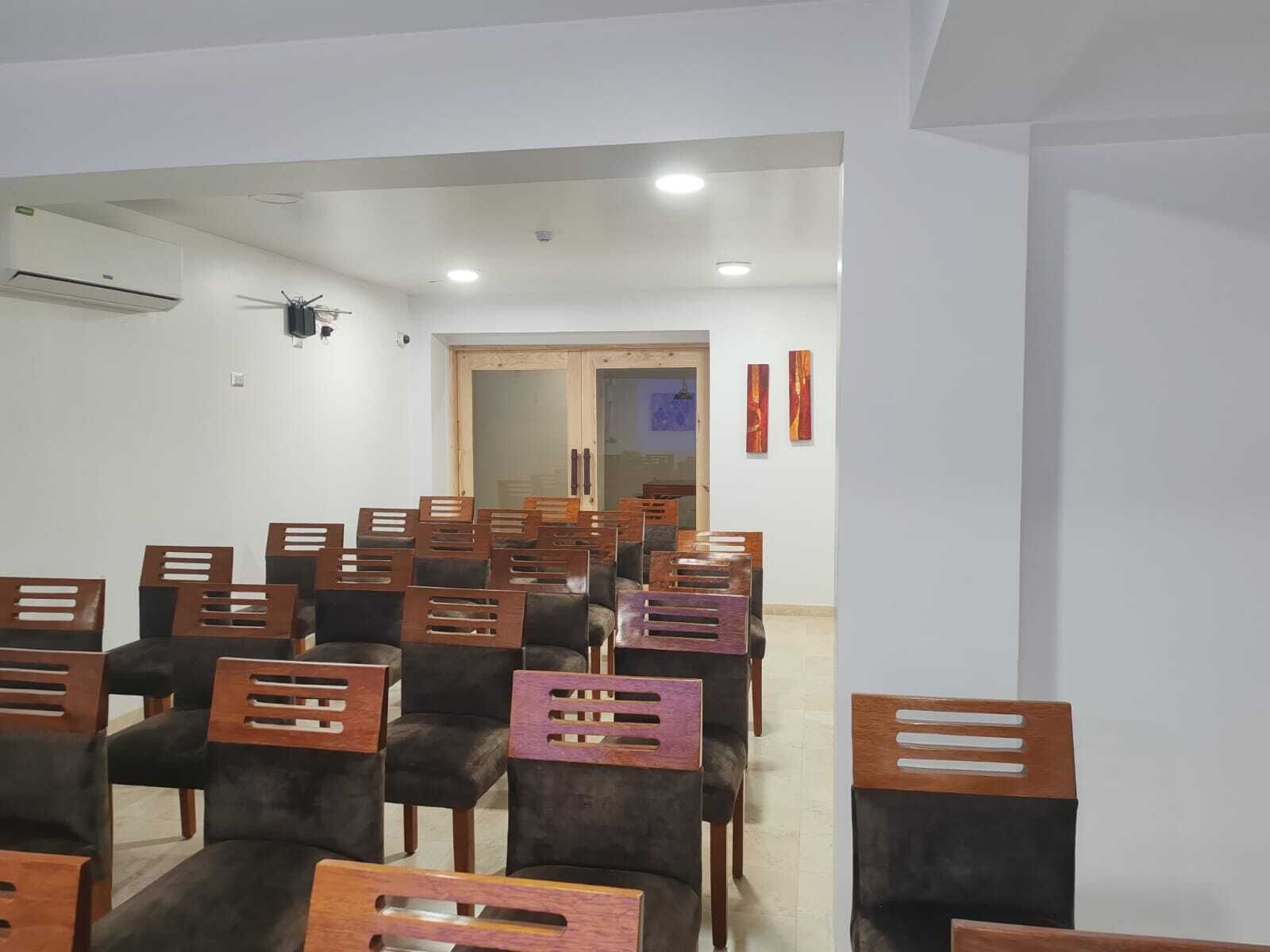 Una sala de conferències amb files de cadires, un aire condicionat i una porta que dona a una altra sala.