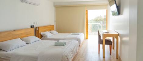 A hotel room with two beds, a desk, a chair, an air conditioning unit, and a television mounted on the wall.