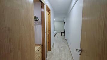Un estrecho pasillo con puertas de madera a ambos lados, que conduce a una habitación con inodoro y una silla.
