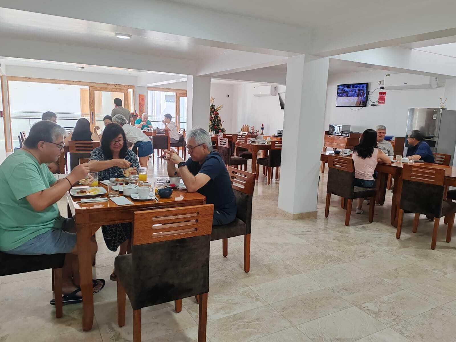 A dining area with multiple tables and chairs, a television mounted on the wall, and a visible fire extinguisher.
