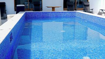 A rectangular swimming pool with blue mosaic tiles, surrounded by a white tiled deck.