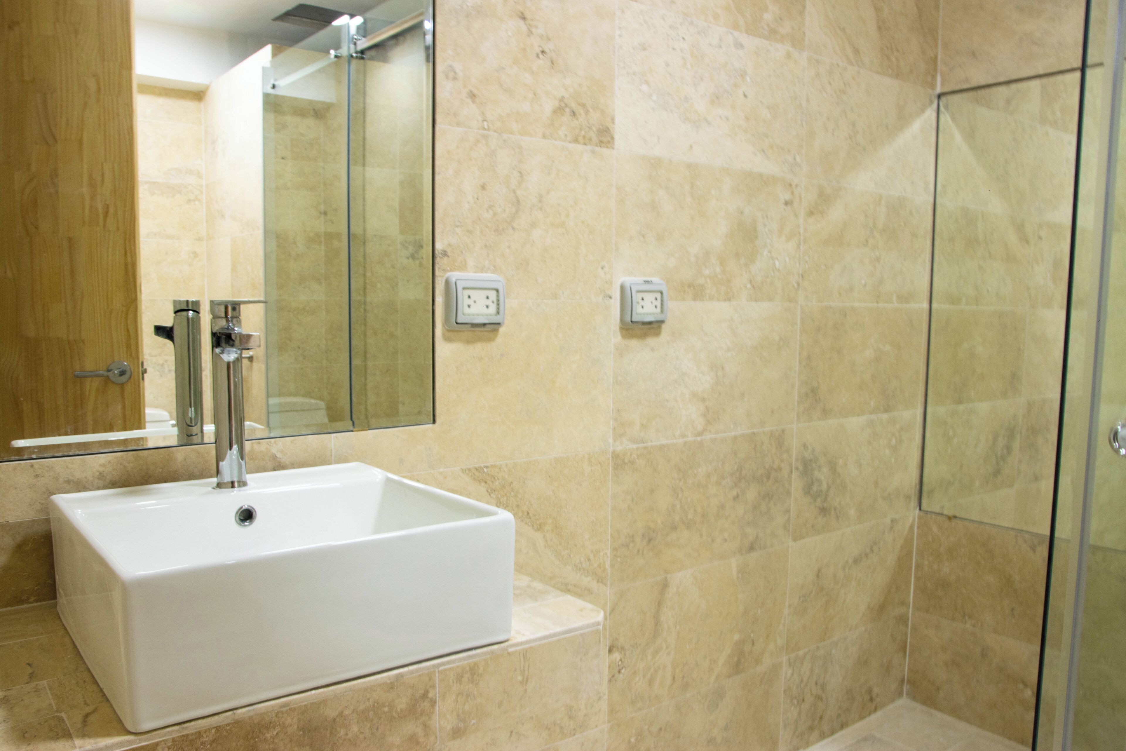 A bathroom with a white sink, a glass shower enclosure, and beige tiled walls.