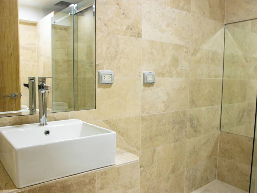A bathroom with a white sink, a glass shower enclosure, and beige tiled walls.