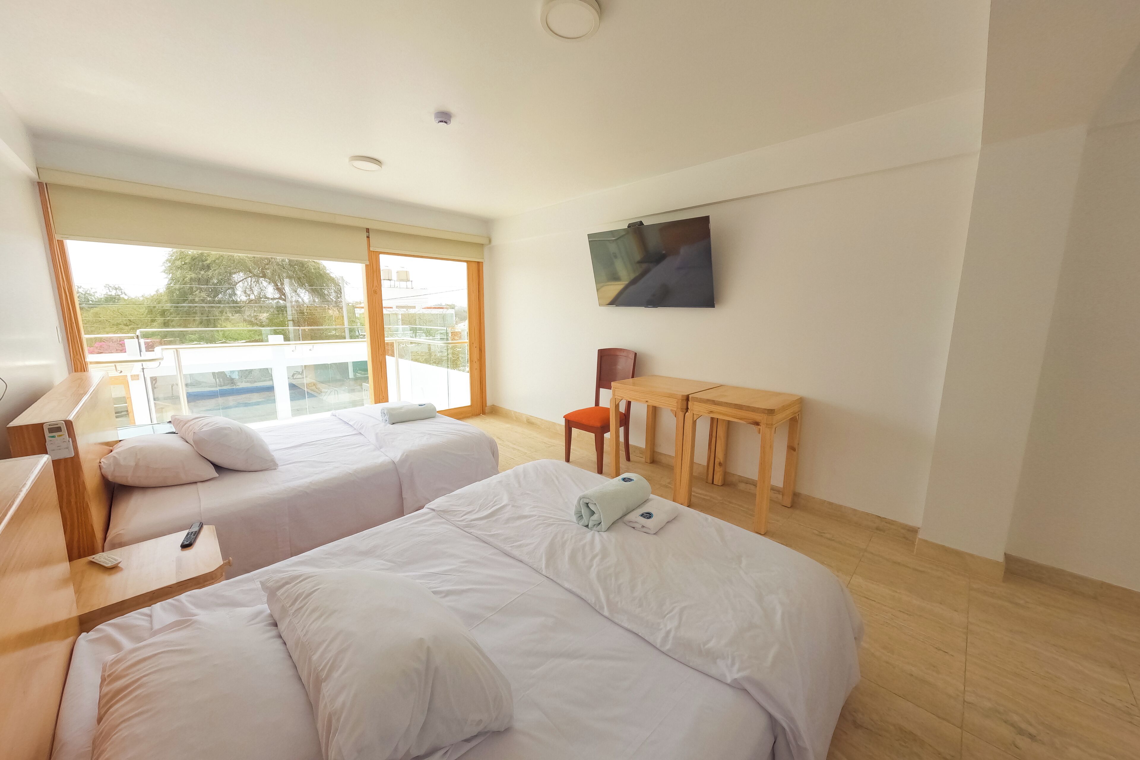Habitación de hotel con dos camas, un escritorio, una silla, televisión y balcón con vistas.