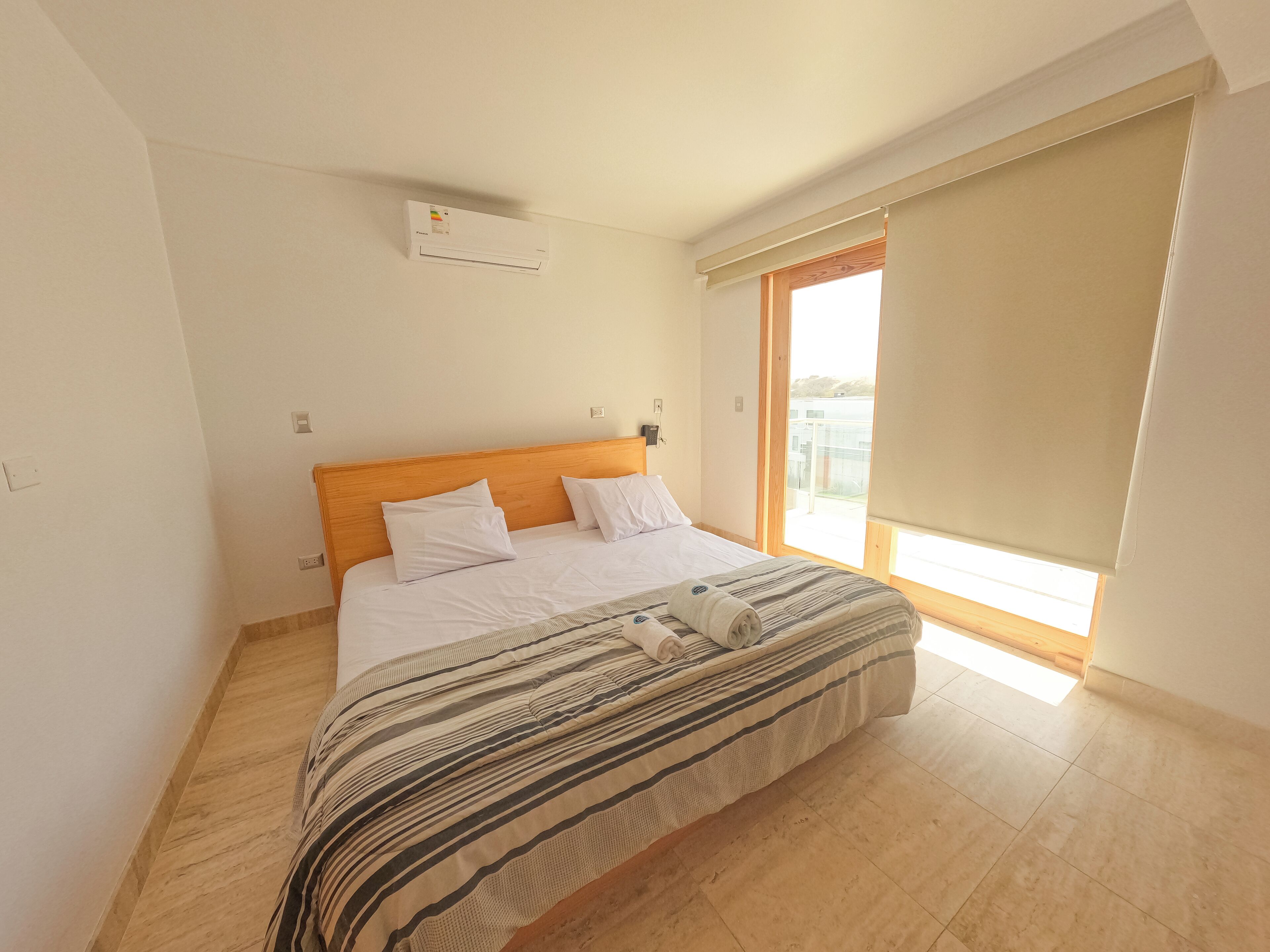 Un dormitorio con cabecera de madera, un ventanal con vistas y una cama con ropa de cama a rayas.