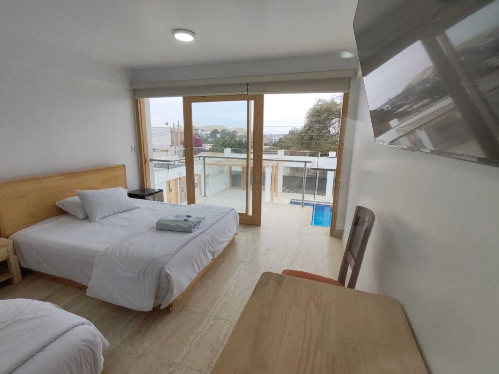 A hotel room with a bed, a small table, a chair, and a balcony with a view of the city.
