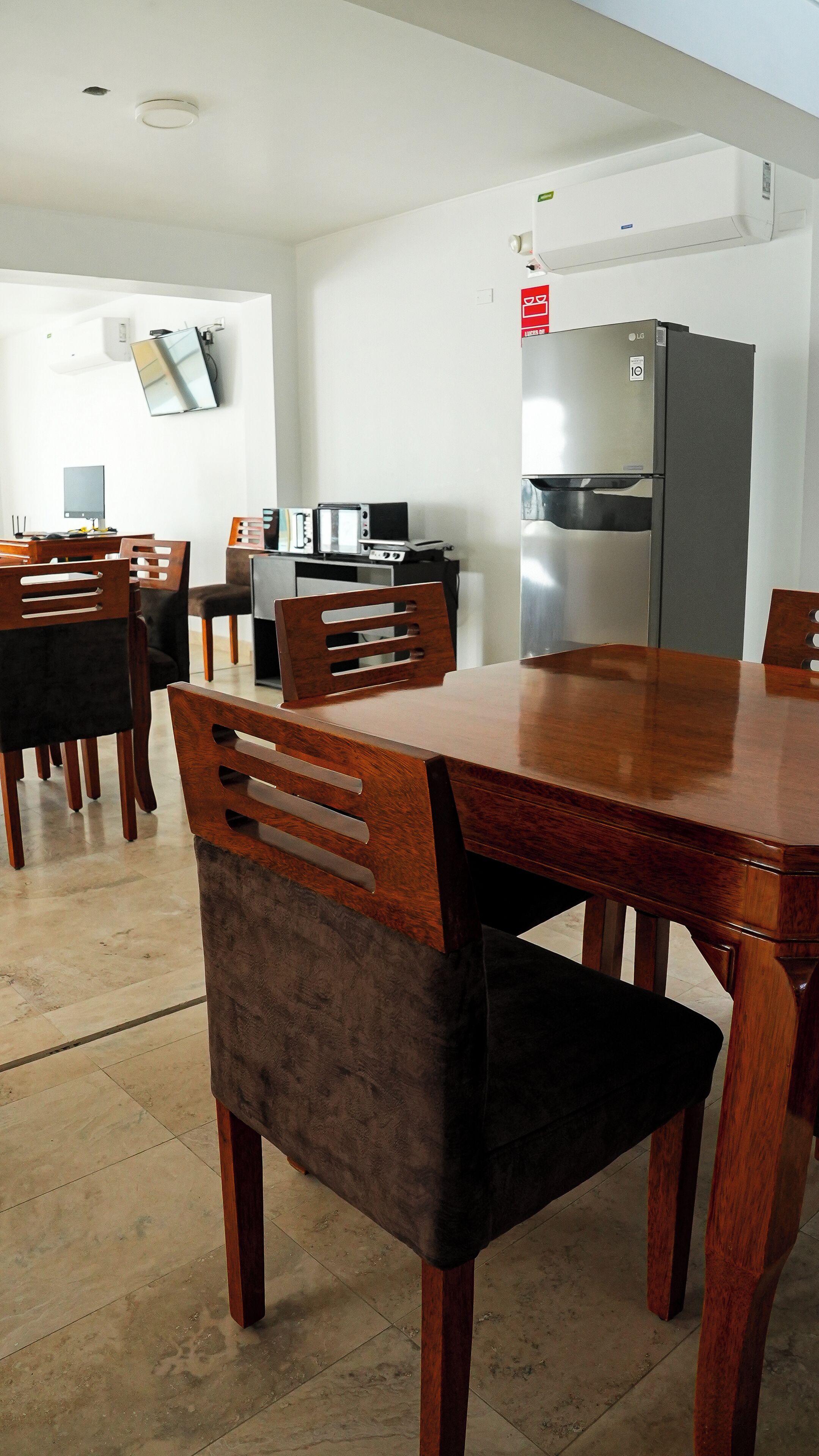 Un coin repas avec une table et des chaises en bois, une cuisine équipée d’un réfrigérateur et un téléviseur à écran plat fixé au mur.