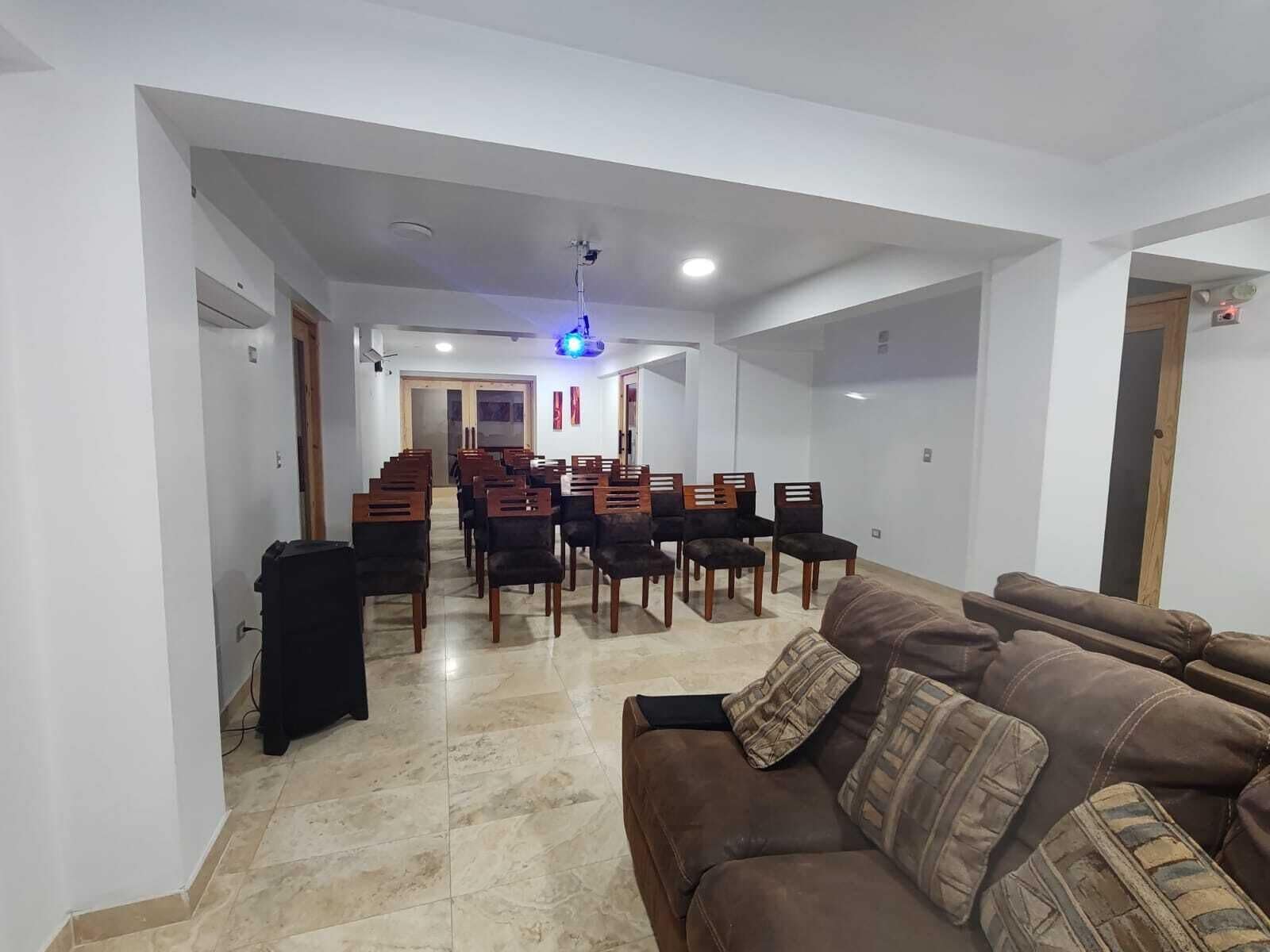 A living room with a brown sofa, a dining area with wooden chairs, and a blue ceiling light.