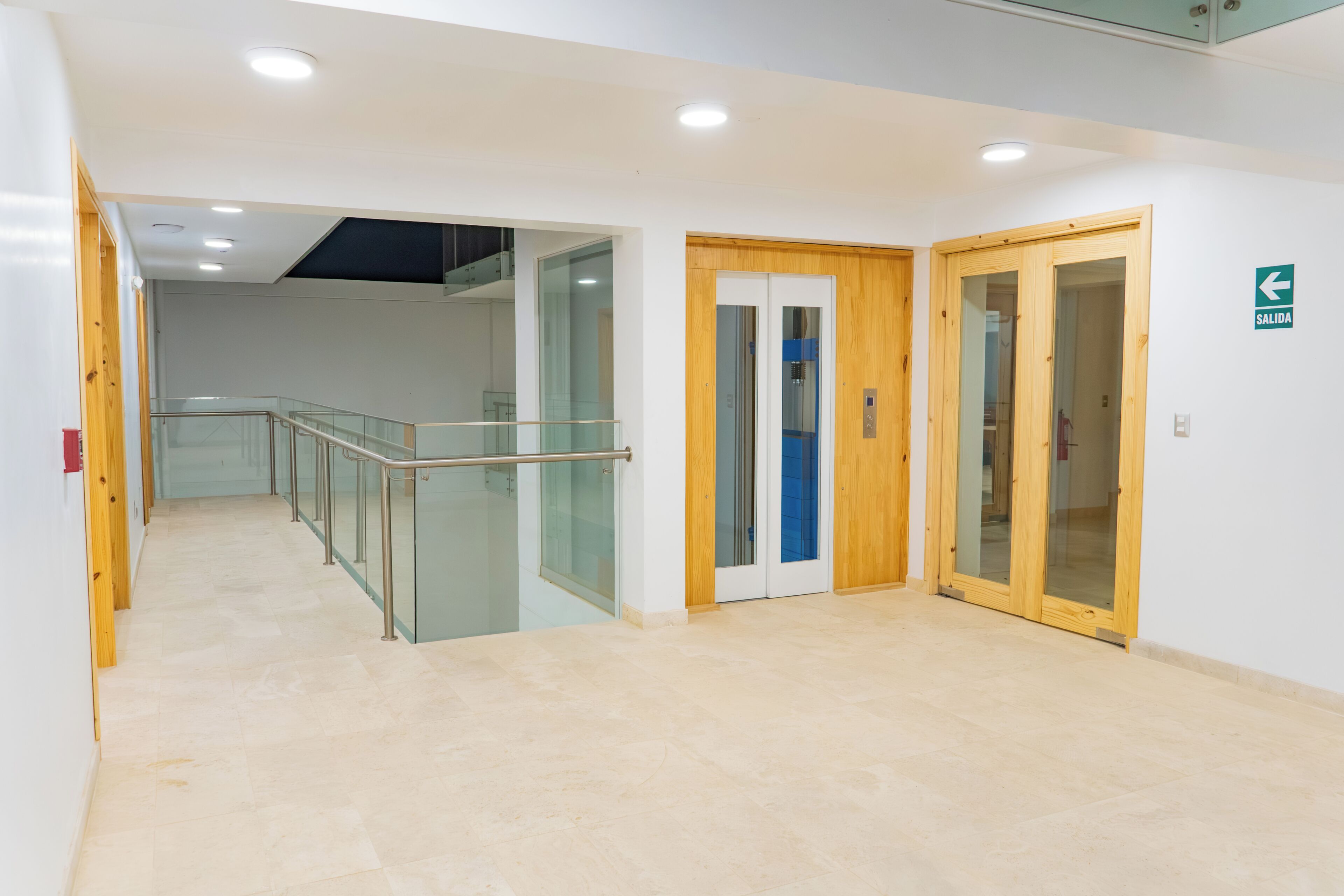 A modern interior with a glass railing, wooden doors, and a clear exit sign.