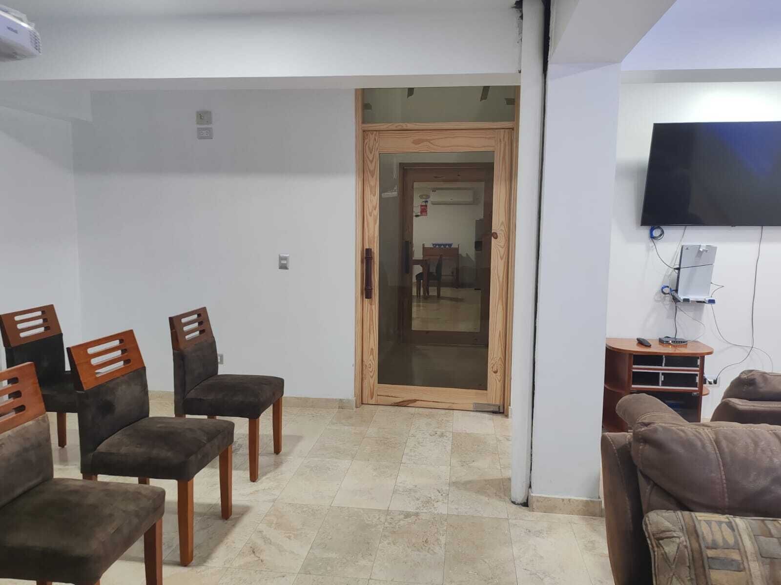 A living room with a television, a wooden door, and a small table with a remote control.