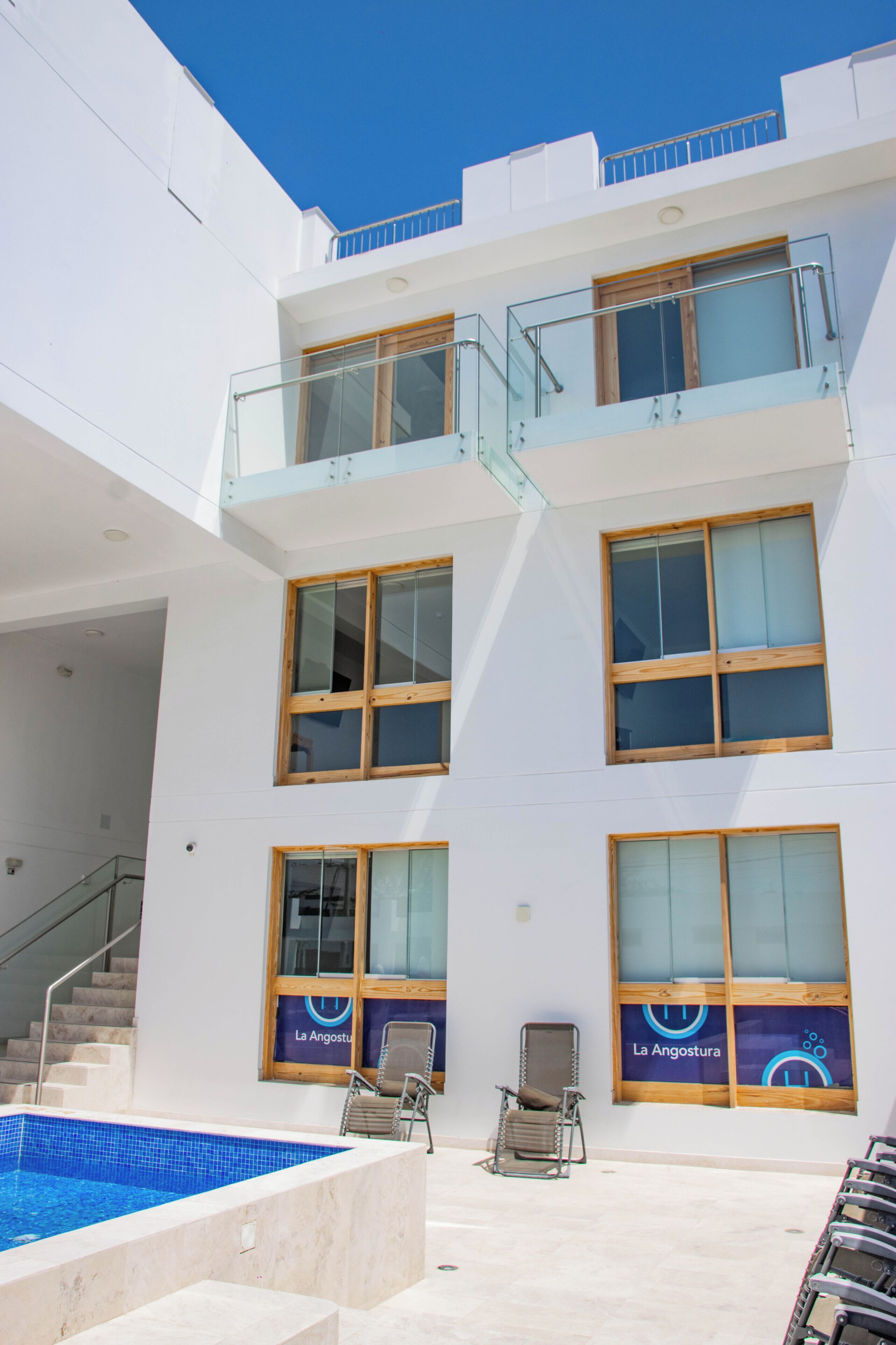 A modern building with a pool, multiple balconies, and a staircase leading to an upper level.