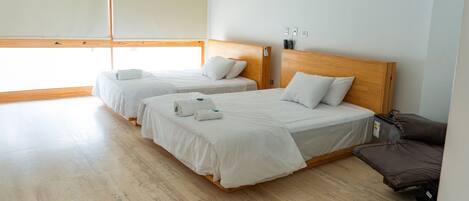 Habitación de hotel con dos camas individuales, un cabecero de madera, una mesita y una ventana con persianas.