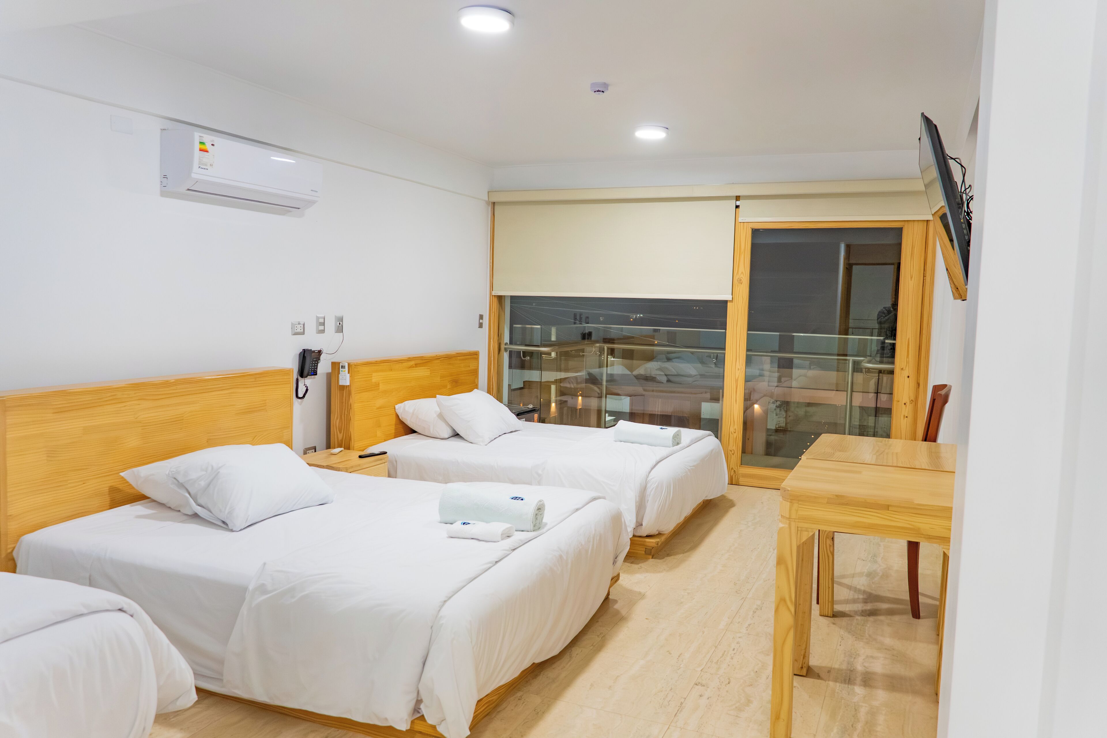 Une chambre d’hôtel avec deux lits, une table en bois, une télévision et un balcon avec une porte vitrée.