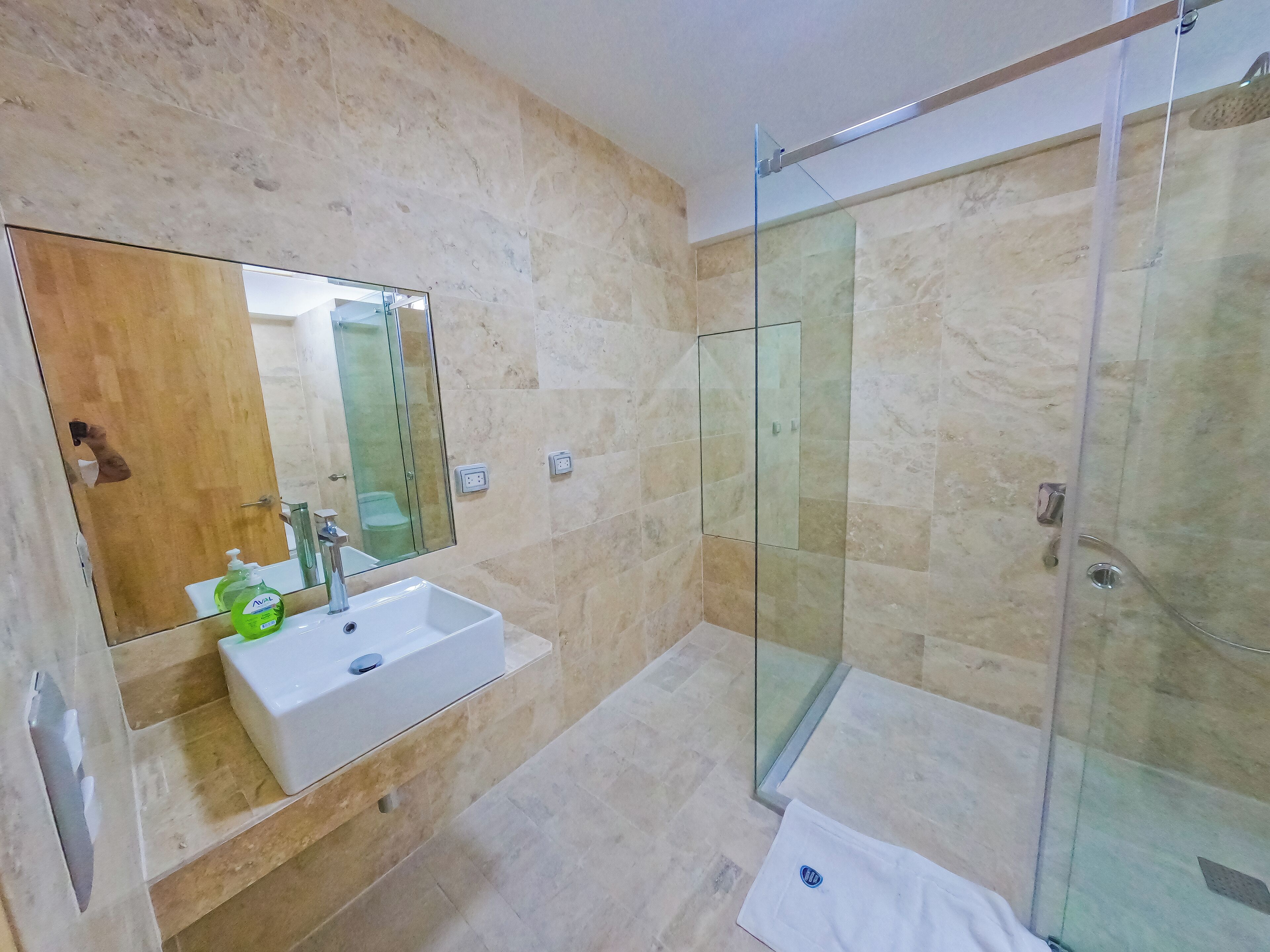 A modern bathroom with a glass shower enclosure, a white sink with a mirror above it, and a towel on the floor.