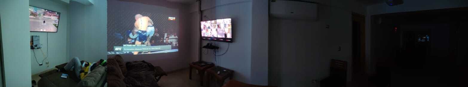 Una stanza con un grande schermo che mostra un videogioco, una televisione e un divano.
