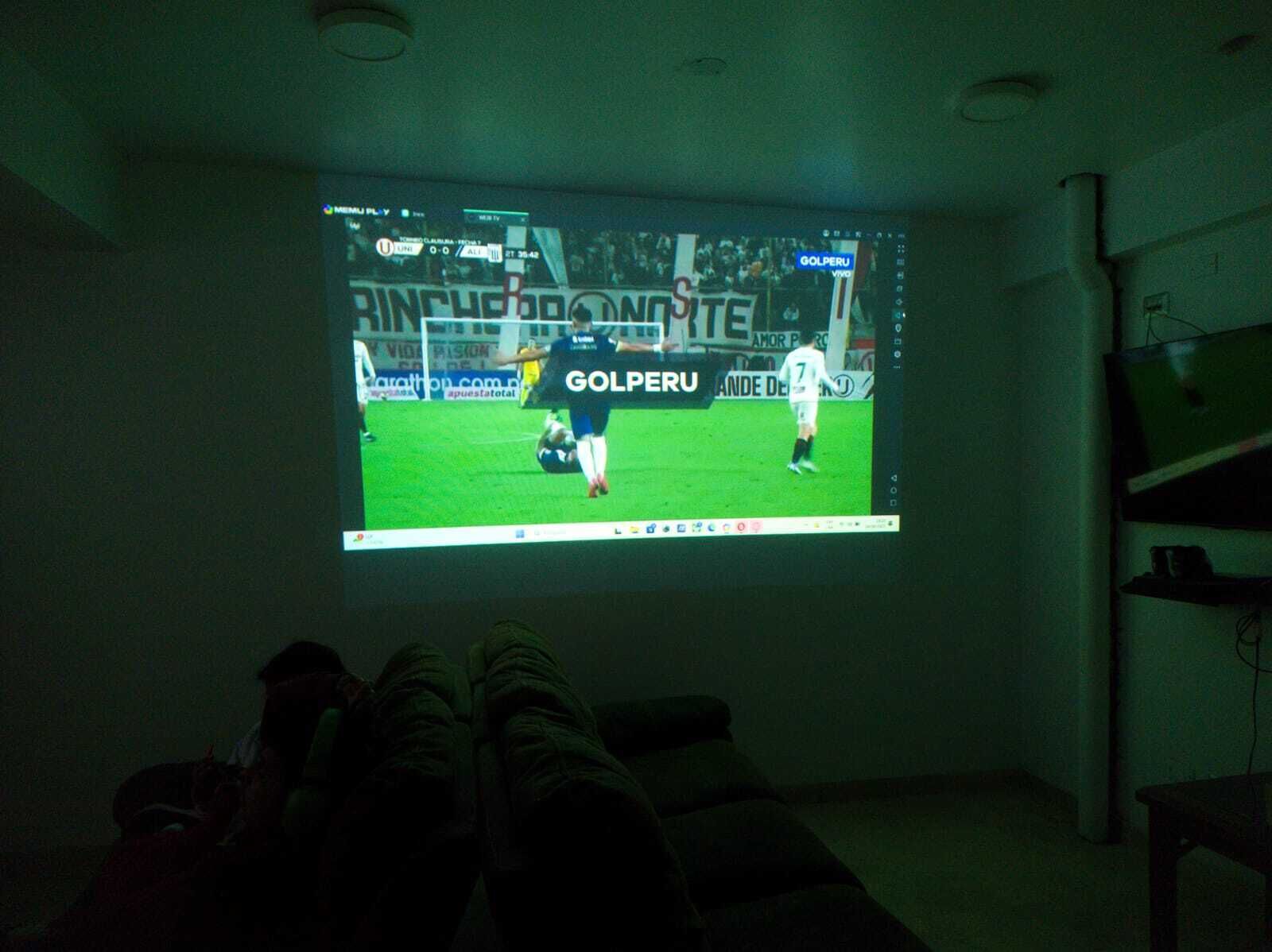 Una pantalla proyectando un partido de fútbol con un jugador con camiseta blanca.
