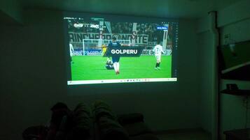 Una pantalla proyectando un partido de fútbol con un jugador con camiseta blanca.
