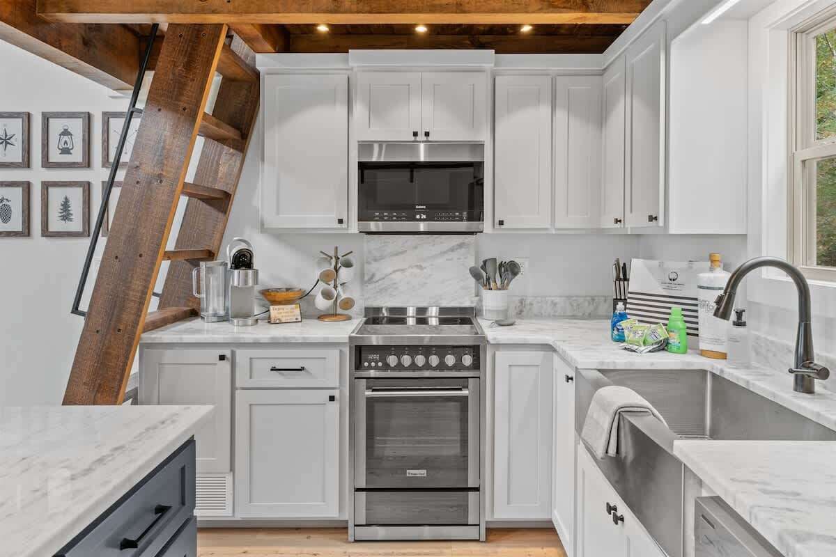 A kitchen with white cabinets, a stainless steel oven, a microwave, and a wooden ladder.