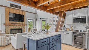A modern kitchen with a stone fireplace, a large island, and a dining area with a sofa. - Sunsets on Garren Cove (Morganton)