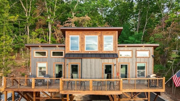 A wooden cabin with a deck, multiple windows, and a flag. - Sunsets on Garren Cove (Morganton)