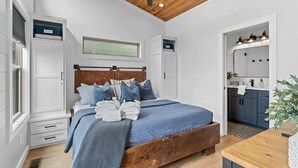 A bedroom with a wooden ceiling fan, a bed with blue bedding, and a view into the bathroom. - Sunsets on Garren Cove (Morganton)