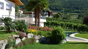 A modern house with a balcony, surrounded by lush gardens and a curved driveway.