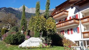 A hotel with a white facade, balconies with wooden railings, and a mountain backdrop.
