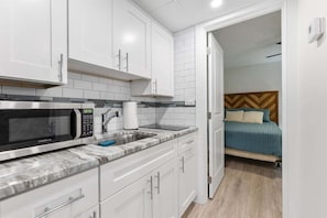 Una cocina compacta con armarios blancos, un microondas y un lavamanos.