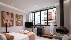 Et moderne hotelværelse med seng, siddeplads, fjernsyn, lille tekøkken og et stort vindue med udsigt.