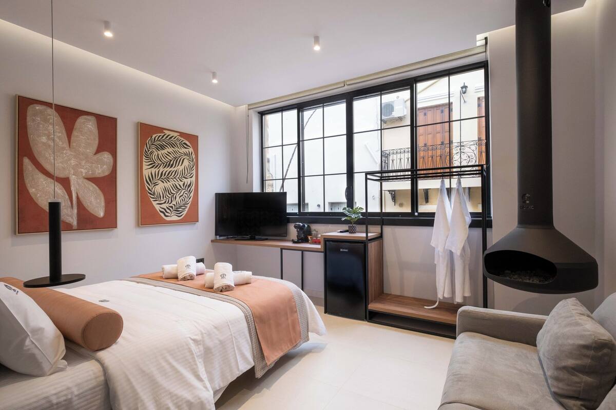 Een moderne hotelkamer met een bed, een zithoek, een televisie, een kitchenette en een groot raam met uitzicht.