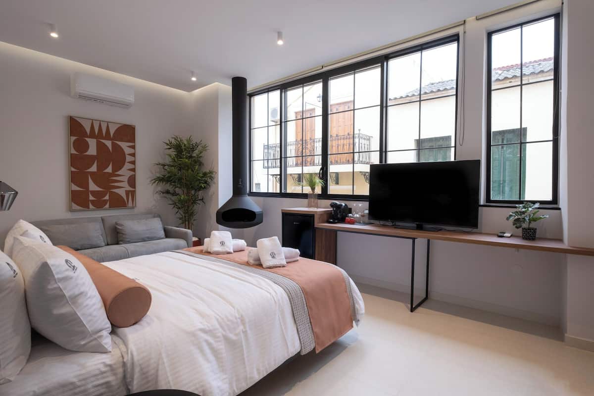 Een moderne slaapkamer met een bed, bureau, televisie en grote ramen.