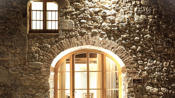 An arched stone doorway leading to a room with a wooden door and windows, flanked by potted plants and a staircase. - Relais La Costa by Interhome (Monteriggioni)