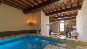 An indoor swimming pool with a tiled edge, wooden beams on the ceiling, and a candelabra with candles. - Relais La Costa by Interhome (Monteriggioni)
