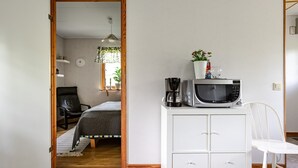 Una habitación compacta con una cama, un mueble blanco con cajones, un microondas y una cafetera.