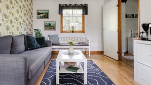 Una sala de estar con un sofá gris, una mesa de centro blanca, un tapete estampado, un ventilador de techo y una ventana con cortinas.