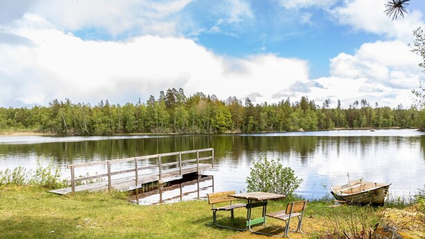 Un parque junto al lago con un muelle de madera, mesas de picnic y un bote.