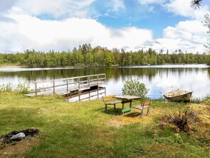 Un parque junto al lago con un muelle de madera, mesas de picnic y un bote.