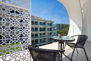 Un balcon doté d’une table en verre et de deux fauteuils en osier, offrant une vue sur un immeuble moderne à plusieurs étages et un ciel dégagé.