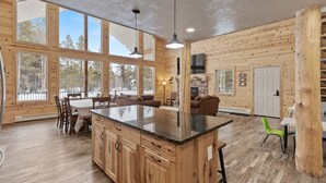 A spacious kitchen with a large island, wooden walls, and large windows offering views of the outdoors. - Grandpa`s Cabin | Sleeps 22, Near Yellowstone, Hot Tub, Family Friendly! (Island Park)