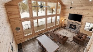 A cabin interior with a large wooden ceiling, a fireplace, a TV mounted above it, and a balcony with a railing. - Grandpa`s Cabin | Sleeps 22, Near Yellowstone, Hot Tub, Family Friendly! (Island Park)