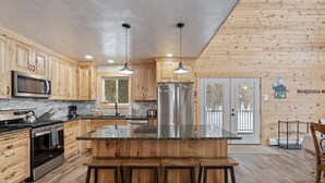A modern kitchen with wooden cabinets, stainless steel appliances, and a central island with bar stools. - Grandpa`s Cabin | Sleeps 22, Near Yellowstone, Hot Tub, Family Friendly! (Island Park)