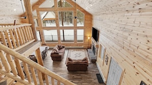 A spacious loft-style room with a high ceiling, large windows, a wooden staircase, and a cozy seating area. - Grandpa`s Cabin | Sleeps 22, Near Yellowstone, Hot Tub, Family Friendly! (Island Park)