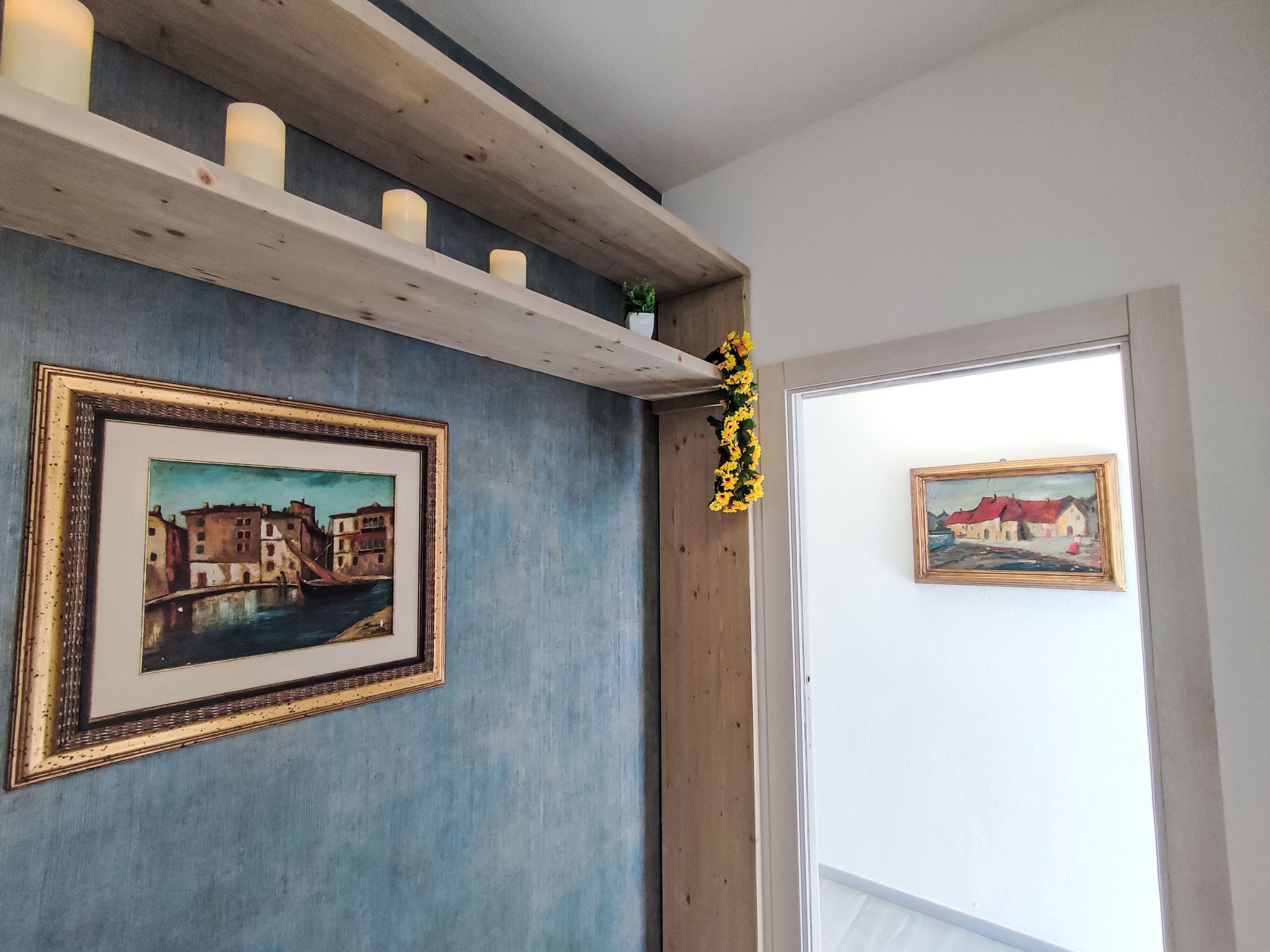 Une pièce avec un mur bleu, des étagères en bois ornées de bougies et deux tableaux encadrés.