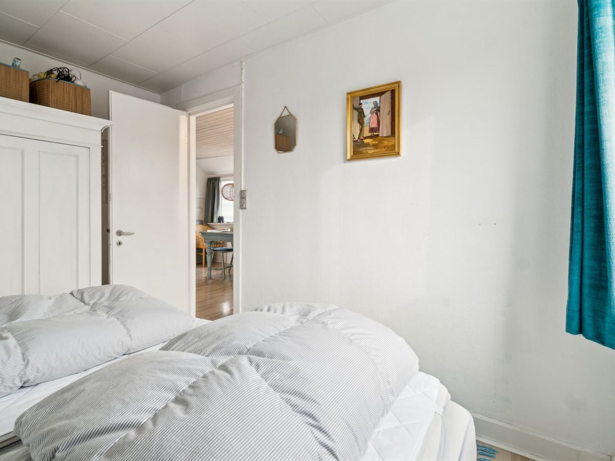 A bedroom with a bed, a door, a small table with chairs, and a wall-mounted picture.