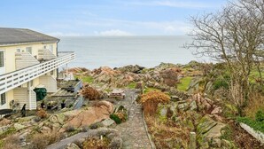 Een pand aan de kust met een stenen pad dat leidt naar een houten terras, met uitzicht op de zee.